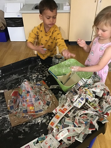Two children pulling newspaper strips out of a bowl filled with flour and water mixture