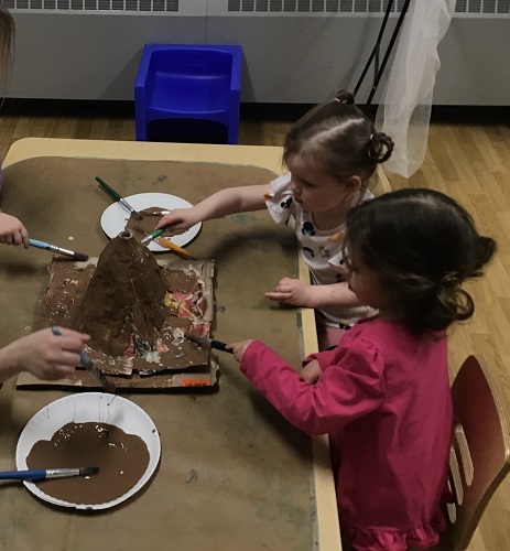 Children sitting at a table painting a volcano they made
