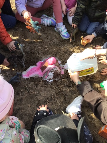 A group of children sitting in the sandbox surrounding a volcano