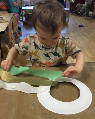 A child sitting at a table sticking long pieces of paper to a cut out paper plate