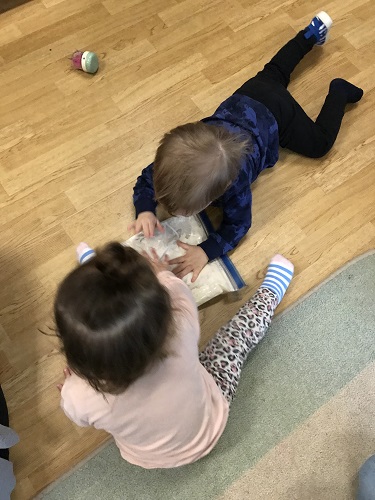 Two children on the ground squishing a ziplock bag filled with ingredients to make dough