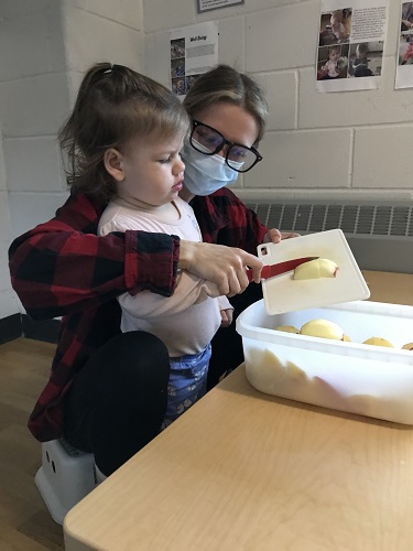 An educator and child cutting pieces of apple
