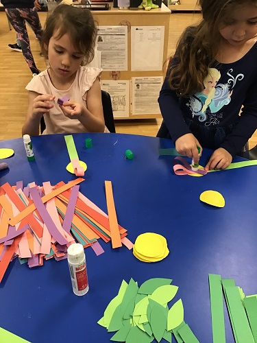 Children sitting at the table using glue sticks on pieces of paper