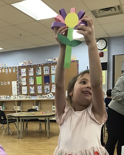 A child holding the flower she made over her head 