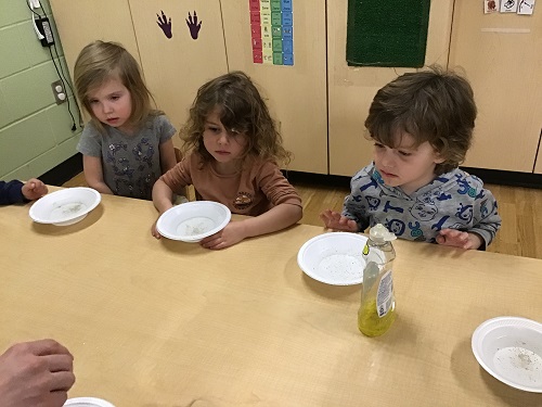 Children sitting at a table with bowls of water in front of them