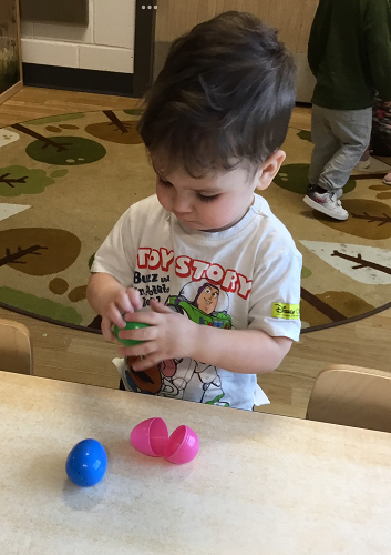 A child at a table looking down at a plastic egg in his hands