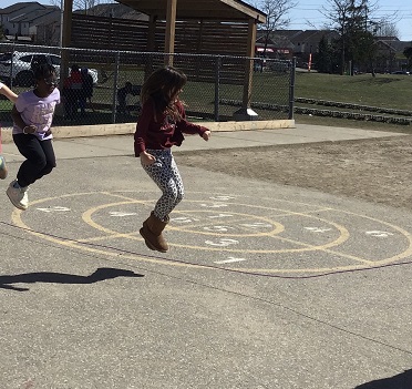 2 children standing in front of each other jumping with a skipping rope