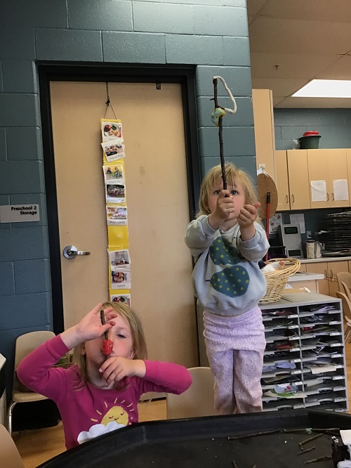 two children holding up sticks that they have decorated with playdough One has some red and the other white playdough
