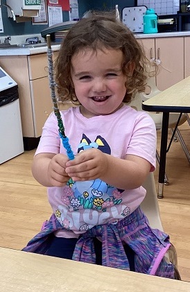girl holding a stick with blue green and grey string wrapped around it