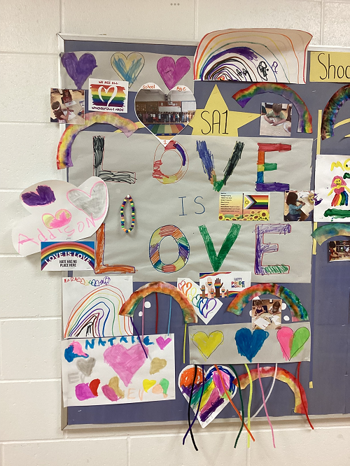 display board with children art work full of rainbows, hearts and a handmade sign that says 'love is love'