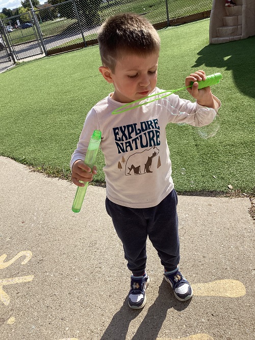 child standing blowing bubbles