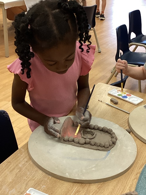 child using an paint brush to paint a clay creation