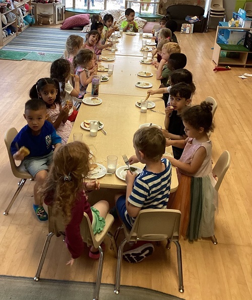 large group of children sitting around a big table have a communal lunch