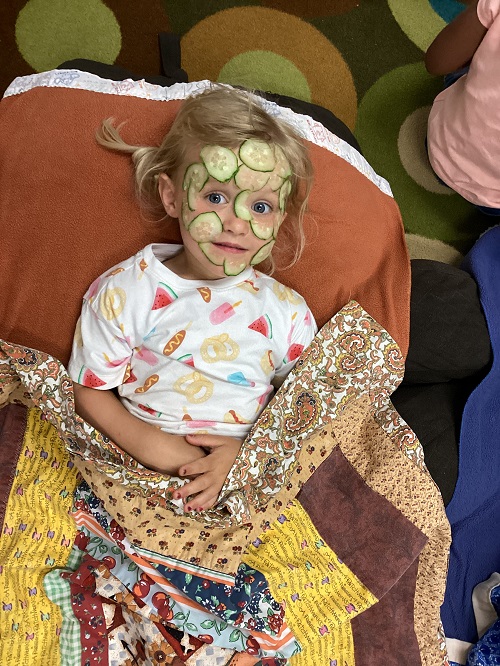 child laying cover in a blanket from the waist up with cucumber slices on her face