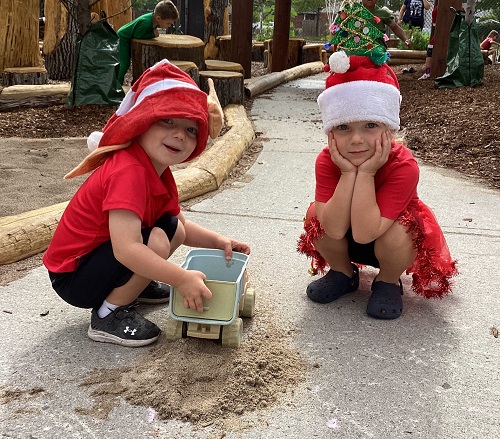 two children crouching down dressed in Christmas costumes with santa claus hats on