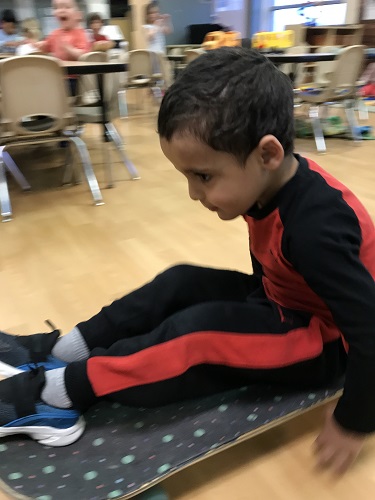 Preschool boy pushing self on skateboard with hands