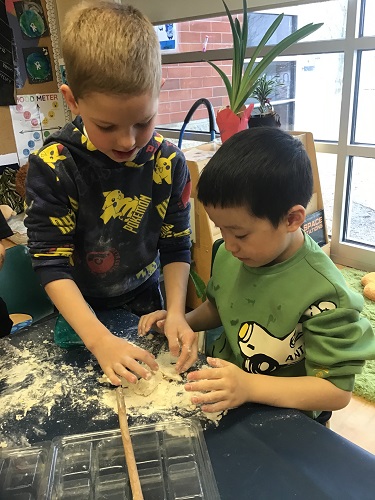 child helping another child with their dough