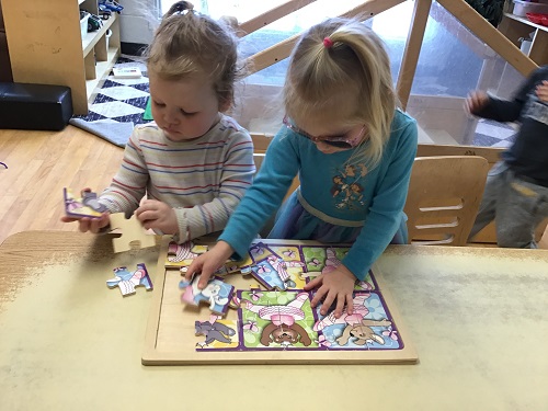 2 preschool children standing at a table working on a puzzle together