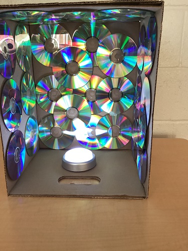 A box decorated with cds on the inside and a puck light sitting at the bottom