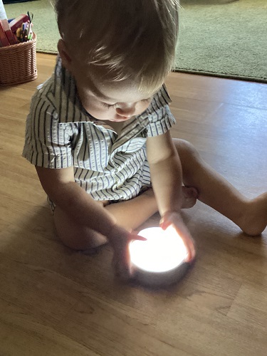 A child sitting on the floor using two hands to push a puck light on