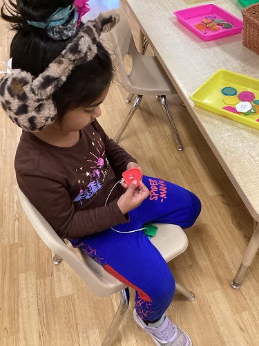 A child at a table adding shapes on a string