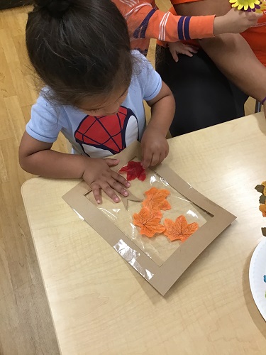A child sitting at a table adding leaves to his artwork