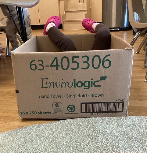 A child's legs sticking out of a large opened cardboard box
