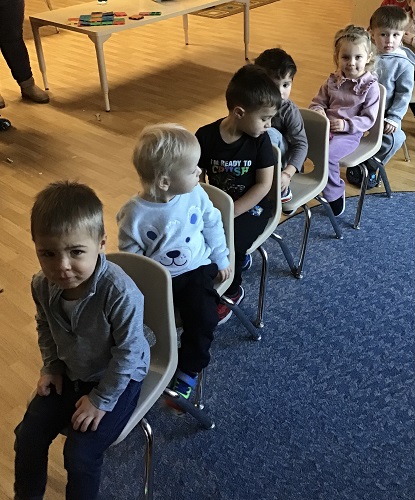 Children lined up sitting on chairs in a row