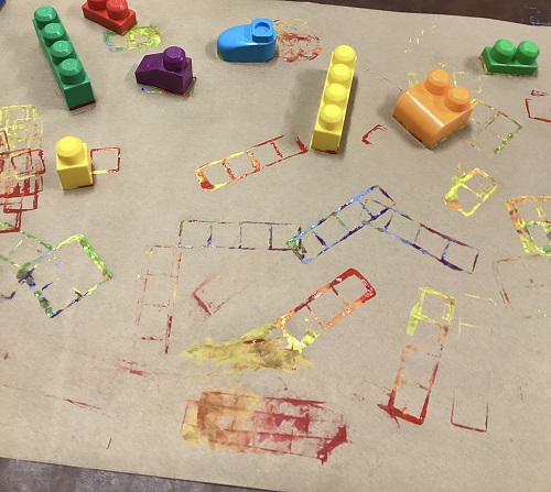 A large paper on a table stamped with Duplo Lego blocks dipped in paint
