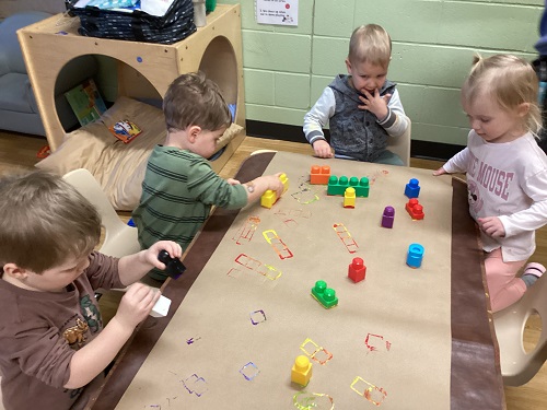 Children at a table stamping Duplo Lego blocks dipped in paint