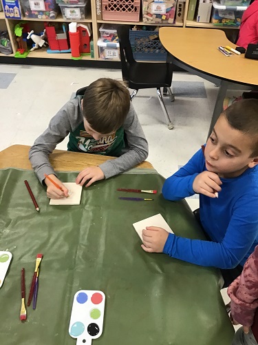 Children at a table painting tiles