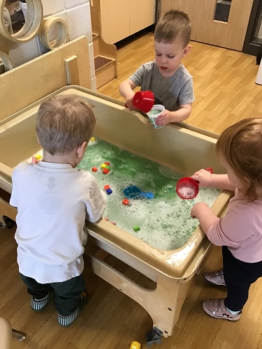 Three children at a sensory bin scooping water with measuring cups
