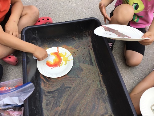 Children sprinkling colourful sand onto glue on a paper plate 