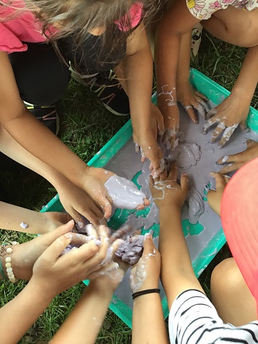 Children surrounding a tray filled with goop