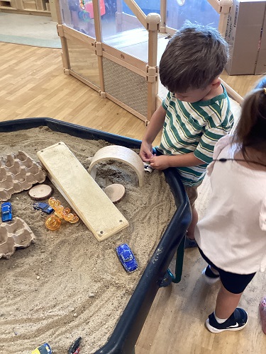 A child at the sand table playign with ramps, blocks and cars