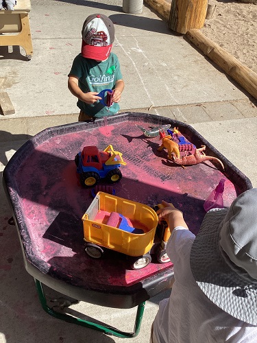 Child standing at the tuff tray with paint and trucks on it
