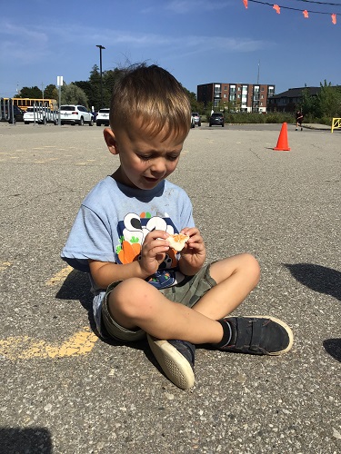 A child sitting on the blacktop with a ball of playdough in their hands