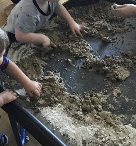 Children playing in the sand and mud mixture in the sensory table