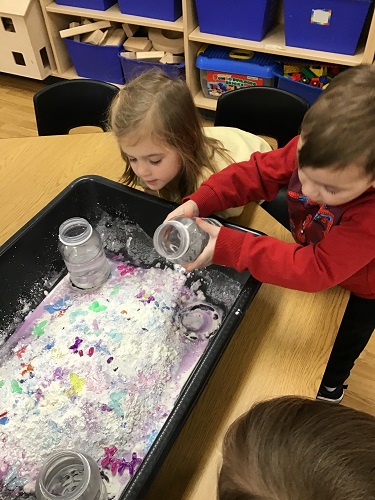Children pouring water into the sensory bin to create oobleck