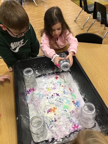 Children pouring water into the sensory bin to create oobleck