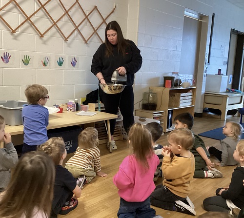 An educator mixing ingredients in a bowl while the children watch