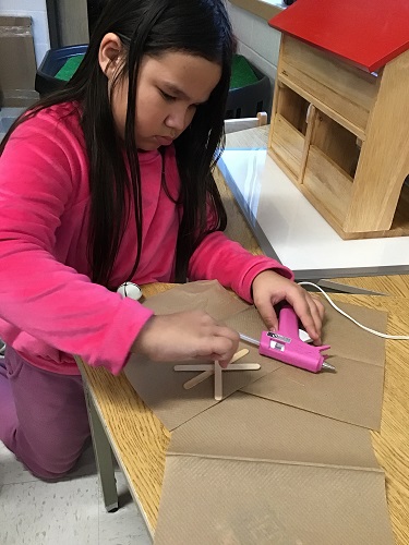 A child using a hot glue gun to make popsicle snowflakes