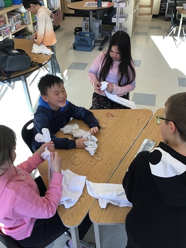 Children at a table using elastics to tie up their shirts