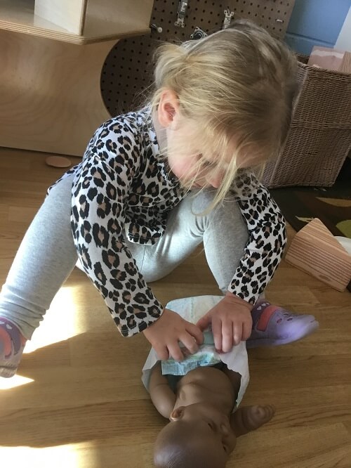 girl putting a diaper on a baby doll