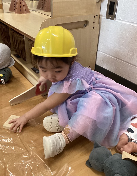 A preschool child holding a pretend saw to cut wood