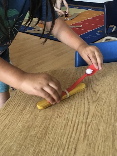 Child holding onto one end of the spoon catapult, one hand on the other end with a pom pom on the spoon ready to catapult
