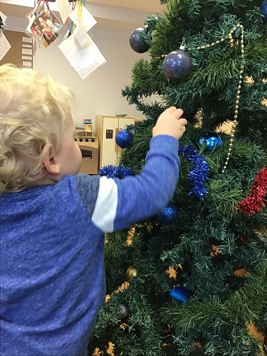 Preschool childing holding a Christmas ball up to the Christmas tree