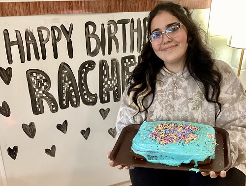 An educator holding a birthday cake standing infront of their birthday wall