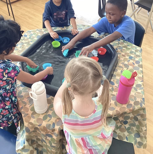 4 children sitting around a tuff tray with silicone molds and water
