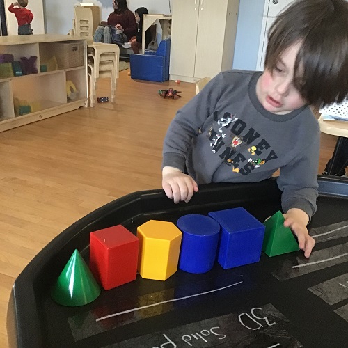 A preschooler is using different shaped blocks to make a pattern.